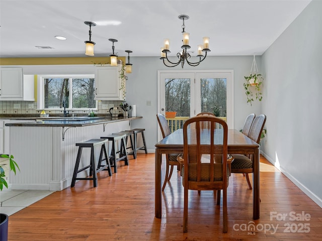 dining space with light wood-style floors, visible vents, a notable chandelier, and baseboards