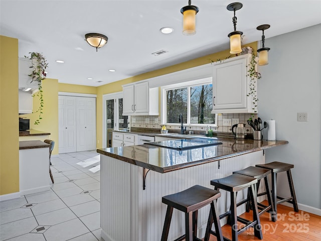 kitchen with pendant lighting, dark countertops, white cabinetry, a peninsula, and a kitchen bar