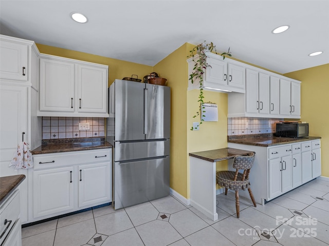 kitchen with black microwave, dark countertops, freestanding refrigerator, and white cabinets