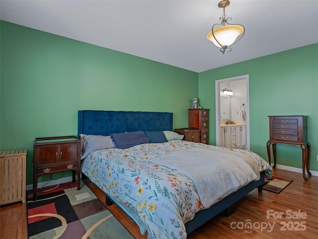 bedroom with baseboards, ensuite bath, radiator heating unit, dark wood-style flooring, and a sink