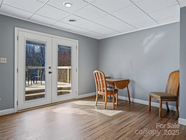 interior space featuring a drop ceiling, wood finished floors, visible vents, baseboards, and french doors