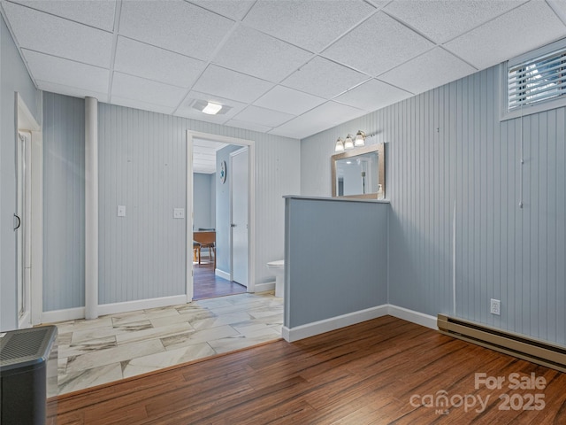 spare room with a drop ceiling, baseboards, baseboard heating, and wood finished floors