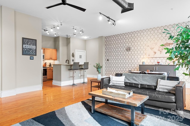 living room with track lighting, ceiling fan, light wood-type flooring, and sink