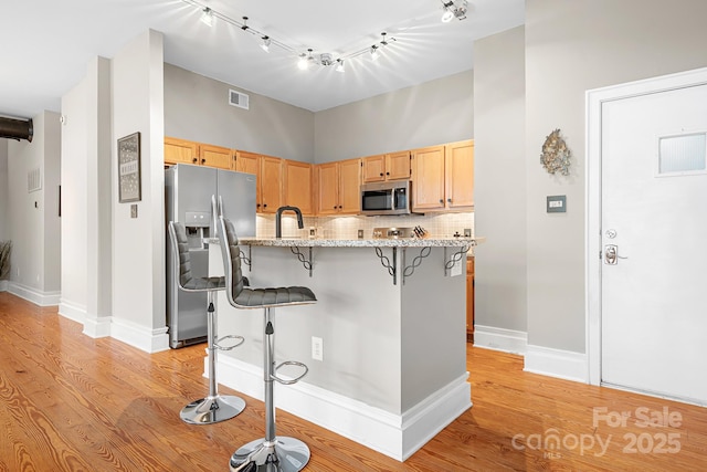 kitchen featuring appliances with stainless steel finishes, light brown cabinets, a kitchen bar, light stone counters, and tasteful backsplash