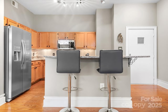 kitchen with a breakfast bar, backsplash, stainless steel appliances, and light stone countertops