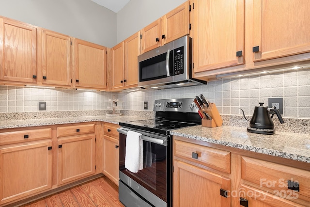 kitchen featuring stainless steel appliances, backsplash, light brown cabinetry, light stone counters, and light hardwood / wood-style flooring