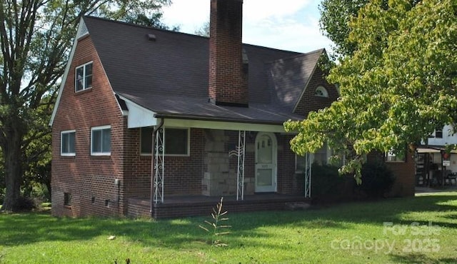 rear view of property with brick siding, a chimney, a porch, and a lawn