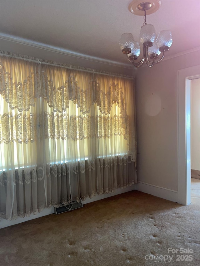 empty room with a chandelier, carpet flooring, crown molding, and baseboards