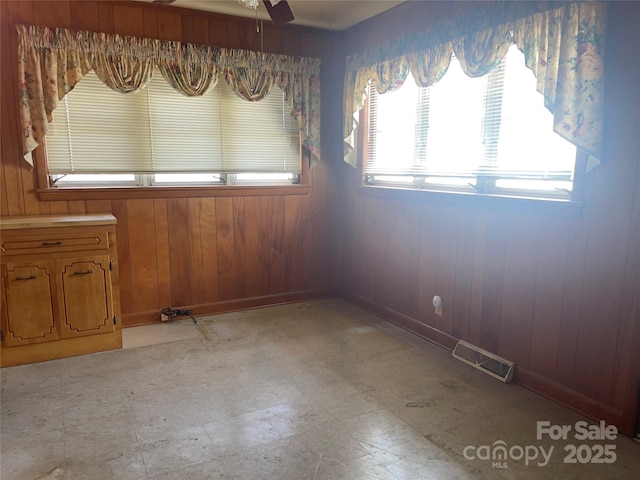 empty room with wooden walls, a ceiling fan, baseboards, visible vents, and light floors