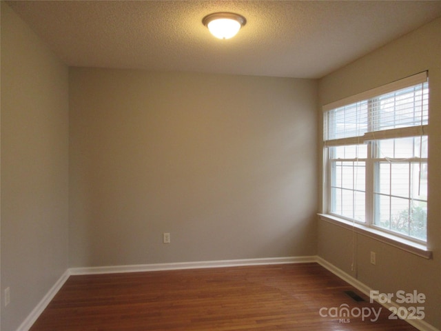 empty room with a textured ceiling and dark wood-type flooring