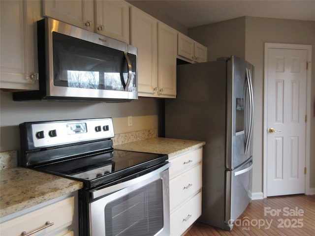 kitchen with stainless steel appliances, light stone countertops, and hardwood / wood-style floors