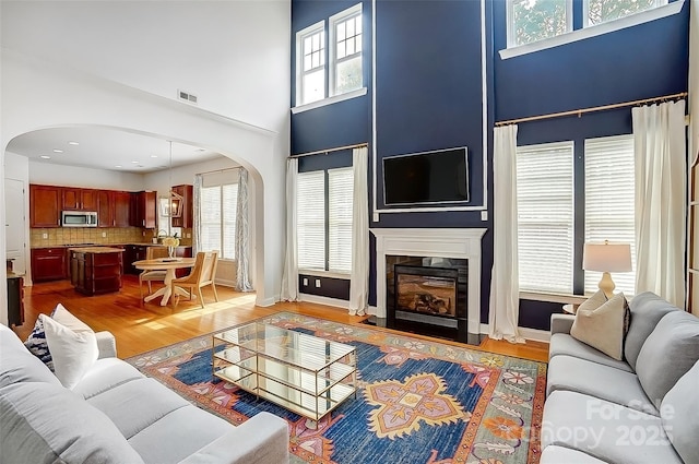 living room featuring arched walkways, light wood-style flooring, a fireplace, visible vents, and baseboards