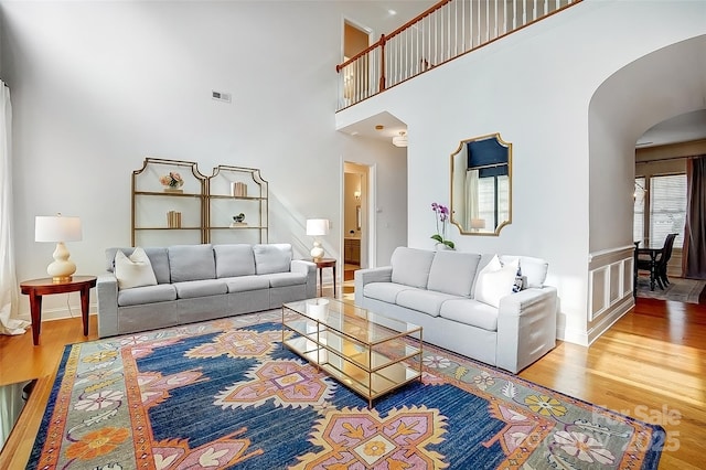 living room featuring visible vents, a high ceiling, arched walkways, and wood finished floors