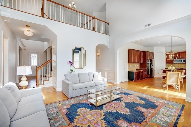 living area featuring light wood finished floors, visible vents, arched walkways, and a notable chandelier