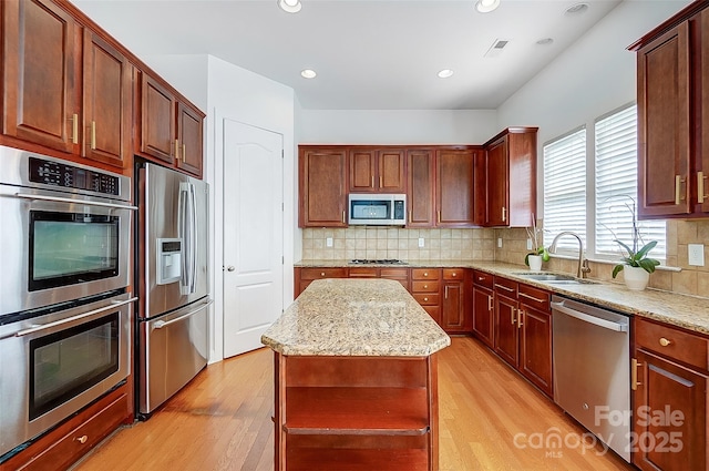 kitchen with light wood finished floors, decorative backsplash, appliances with stainless steel finishes, a center island, and a sink