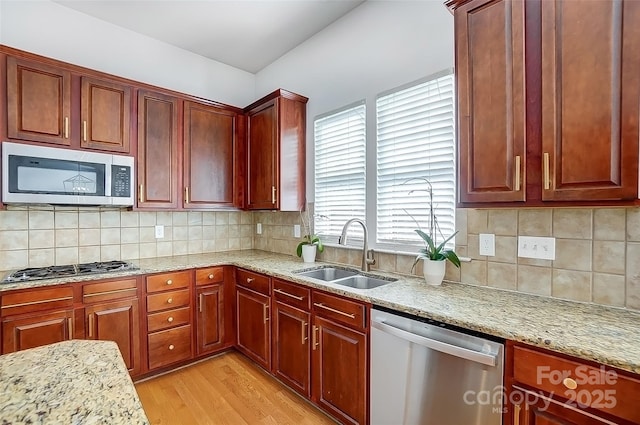 kitchen featuring light stone counters, light wood finished floors, stainless steel appliances, backsplash, and a sink