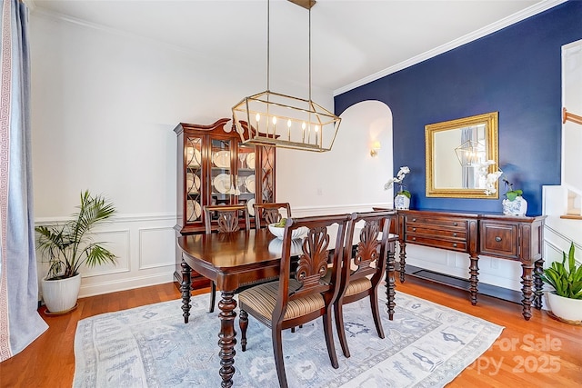 dining area with ornamental molding, a wainscoted wall, a notable chandelier, and wood finished floors