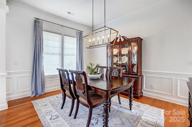 dining space with light wood-style floors, wainscoting, a notable chandelier, and ornamental molding