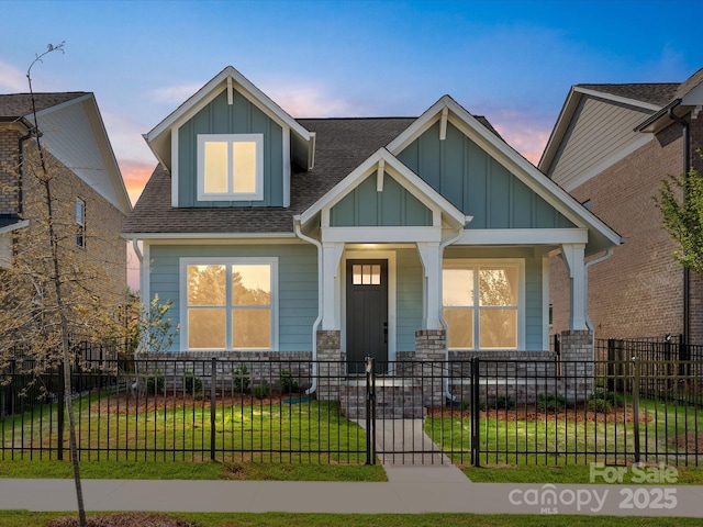 craftsman-style home with board and batten siding, a fenced front yard, a yard, a porch, and roof with shingles