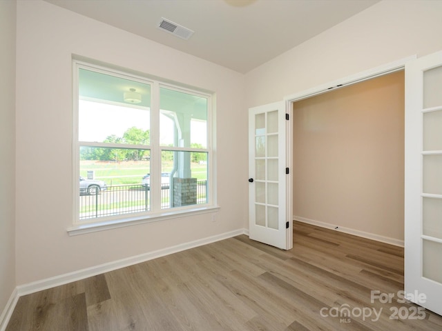 empty room with french doors, visible vents, baseboards, and wood finished floors