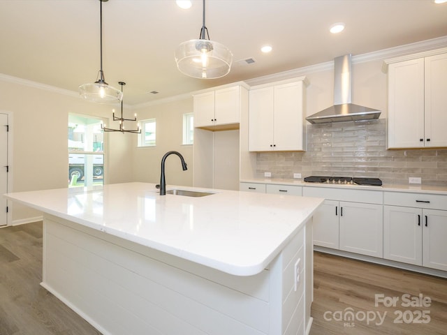 kitchen with black electric stovetop, light wood-type flooring, wall chimney exhaust hood, and a sink
