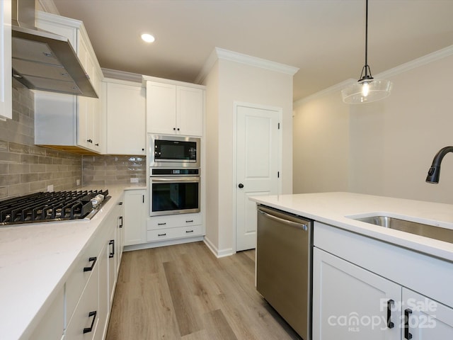 kitchen with wall chimney range hood, ornamental molding, white cabinets, stainless steel appliances, and decorative backsplash