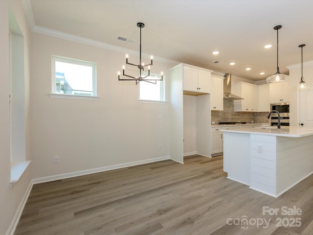kitchen featuring visible vents, a sink, wall chimney range hood, crown molding, and light wood finished floors