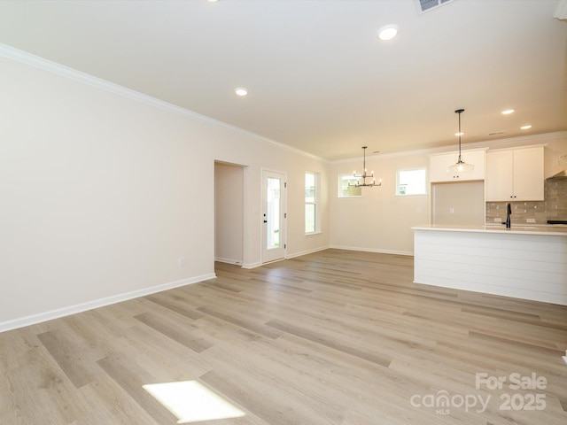 unfurnished living room with ornamental molding, baseboards, a notable chandelier, and light wood-style floors