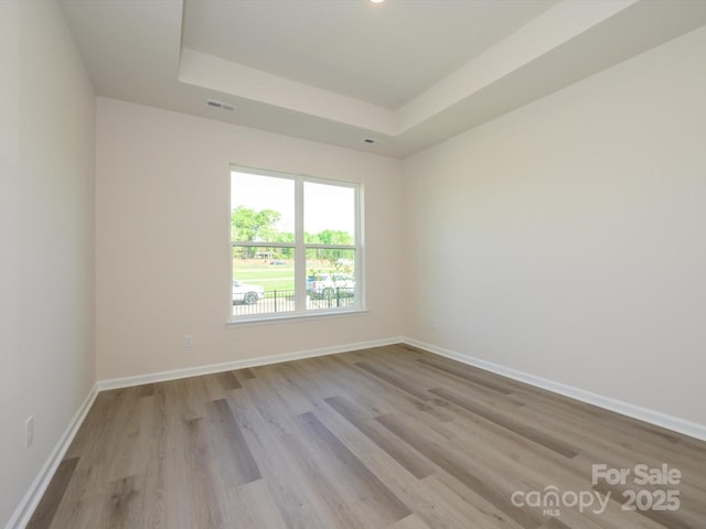 unfurnished room featuring visible vents, baseboards, a raised ceiling, and wood finished floors