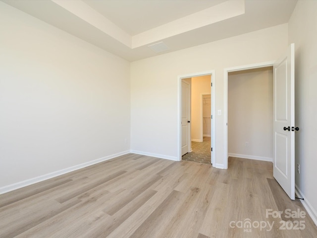 unfurnished bedroom with a tray ceiling, baseboards, and light wood finished floors
