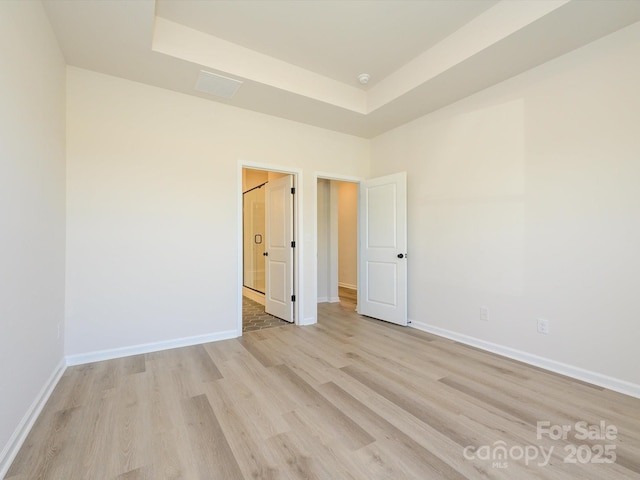 empty room featuring a tray ceiling, baseboards, and light wood-style floors
