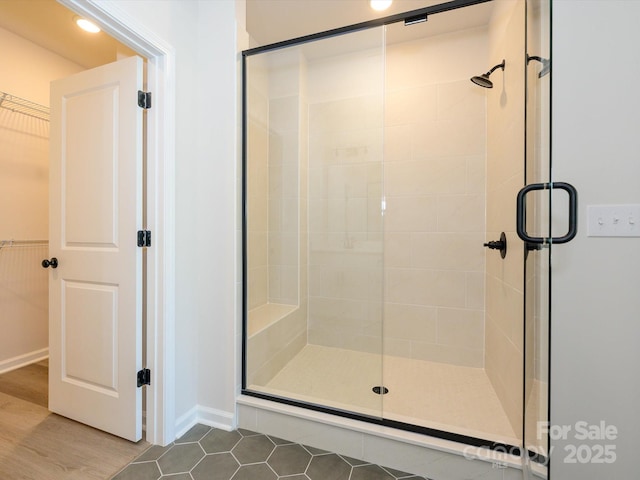 bathroom featuring a walk in closet, baseboards, and a stall shower