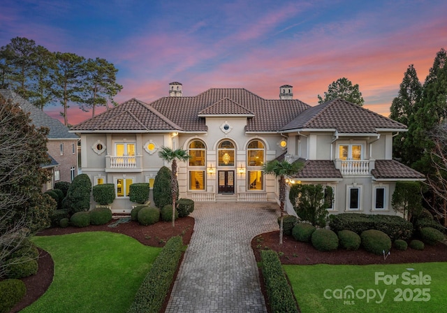 mediterranean / spanish home featuring decorative driveway, a chimney, a tile roof, and a balcony