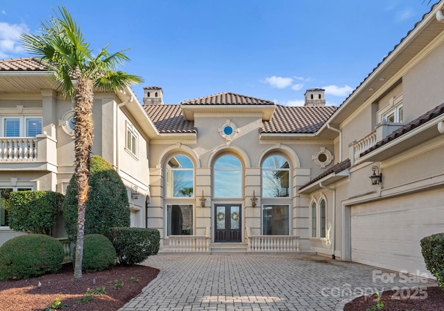 exterior space featuring a garage, a tile roof, french doors, decorative driveway, and a chimney