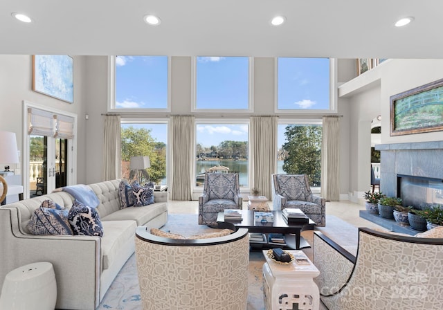 living area featuring a wealth of natural light, a water view, a tiled fireplace, and recessed lighting