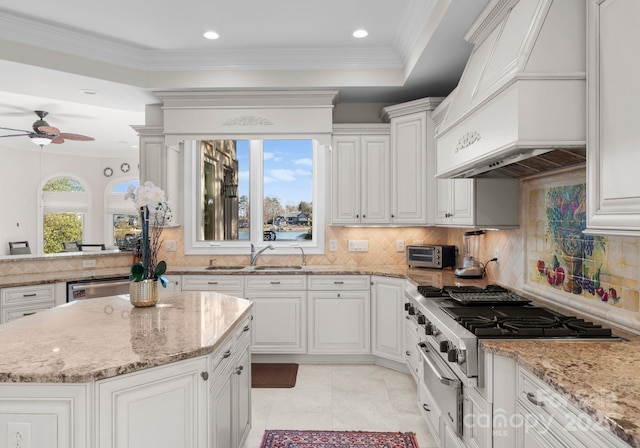 kitchen featuring light stone counters, custom range hood, a sink, and white cabinetry