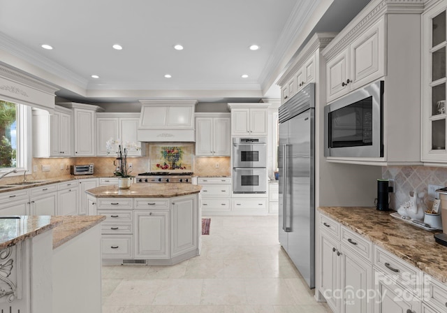 kitchen with built in appliances, white cabinetry, a center island, glass insert cabinets, and custom range hood