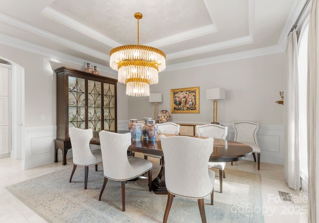 dining space with an inviting chandelier, visible vents, a raised ceiling, and a decorative wall