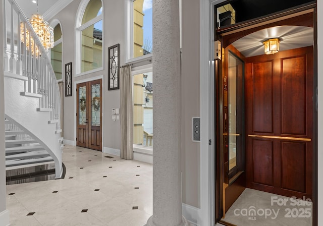 entrance foyer featuring a notable chandelier, baseboards, ornamental molding, stairway, and elevator