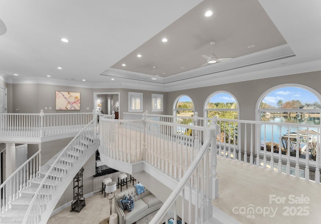 interior space with a tray ceiling, crown molding, recessed lighting, a water view, and an upstairs landing