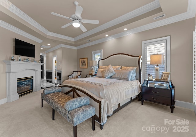 bedroom featuring light carpet, visible vents, a tray ceiling, and a glass covered fireplace