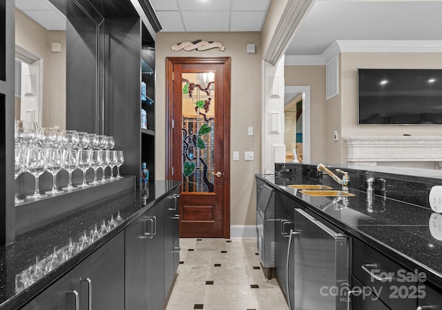 kitchen featuring ornamental molding, a sink, dark stone countertops, dark cabinetry, and baseboards