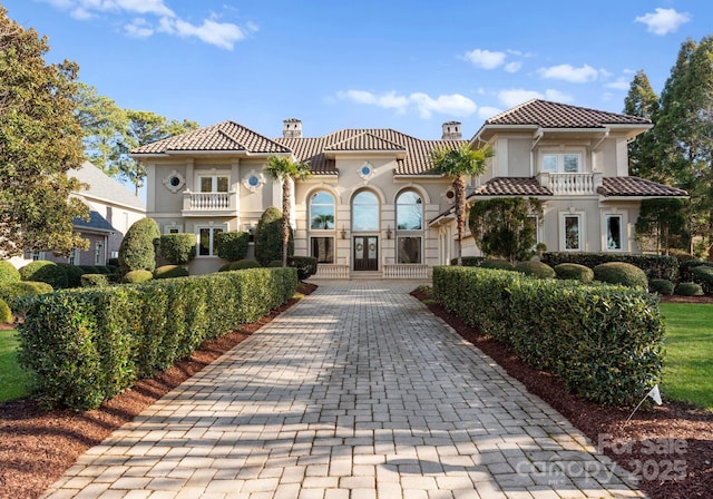 mediterranean / spanish house with french doors, a chimney, stucco siding, a balcony, and a tiled roof