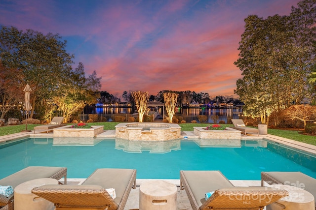 pool at dusk featuring a pool with connected hot tub and fence