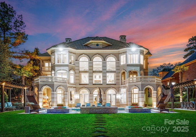 back of property at dusk featuring a yard, stairway, a chimney, and a balcony