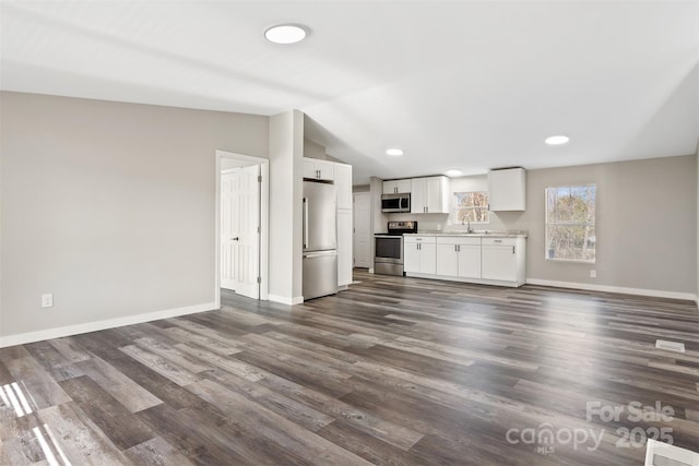 unfurnished living room featuring lofted ceiling, dark wood-style floors, baseboards, and a sink