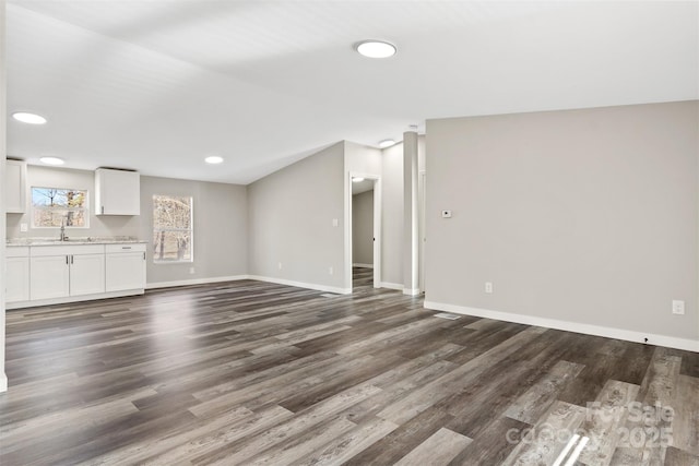 unfurnished living room with dark wood-type flooring, recessed lighting, a sink, and baseboards