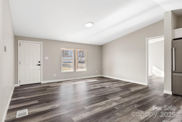 interior space featuring dark wood-type flooring, lofted ceiling, visible vents, and baseboards