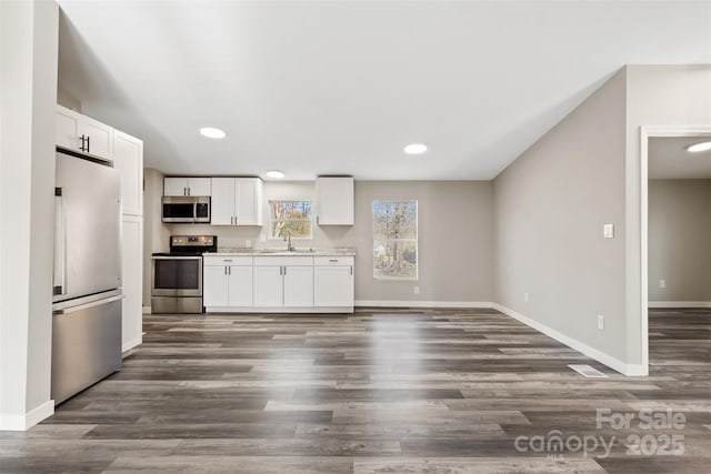 kitchen featuring dark wood-style flooring, stainless steel appliances, white cabinets, a sink, and baseboards