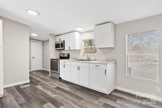 kitchen with baseboards, appliances with stainless steel finishes, a sink, and white cabinets